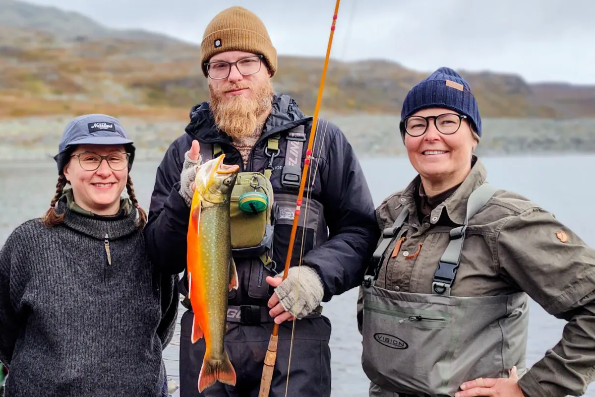Three anglers smiling with a bright red Arctic char