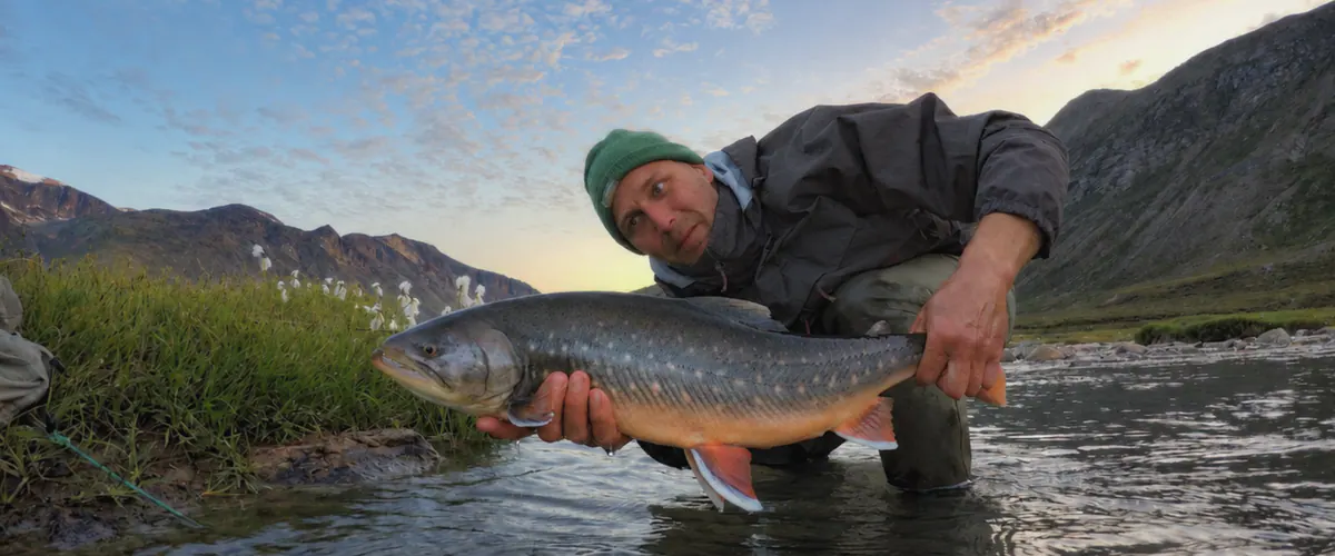 Angler holding an Arctic char by a fell lake at dusk