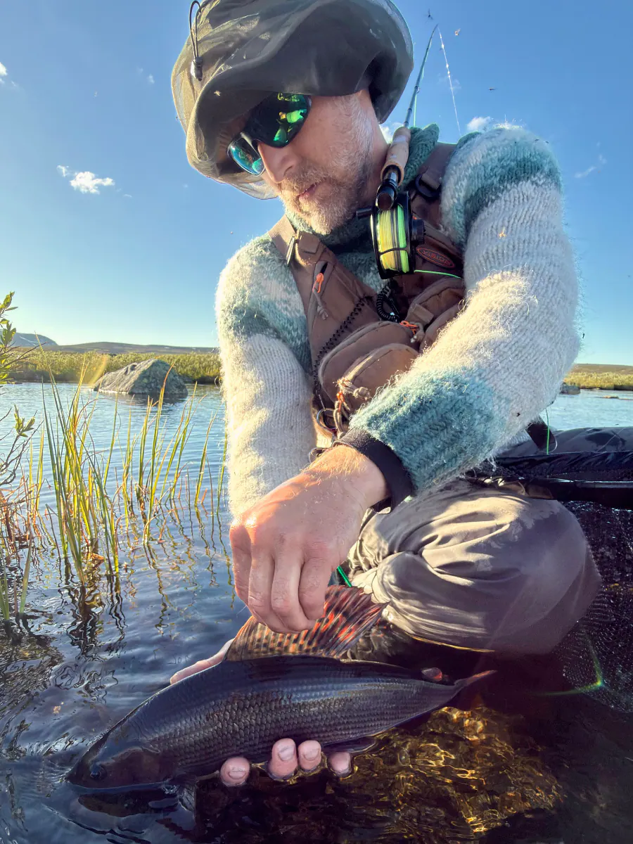 Teemu holding a fly line by a reed-lined lake