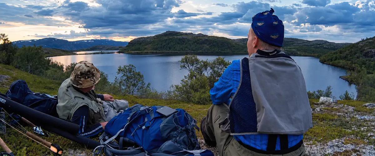 Two anglers resting by a lake with their gear