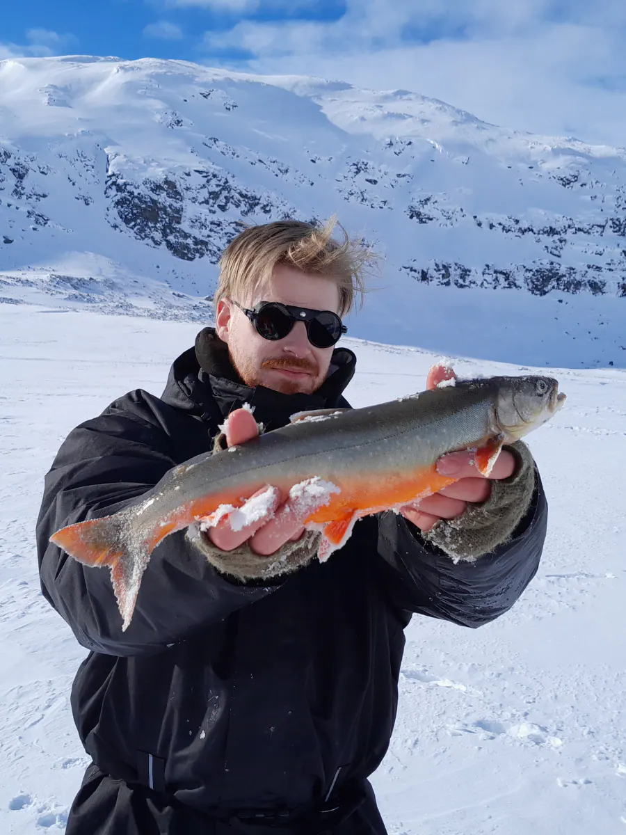 Angler holding a bright Arctic char on the ice
