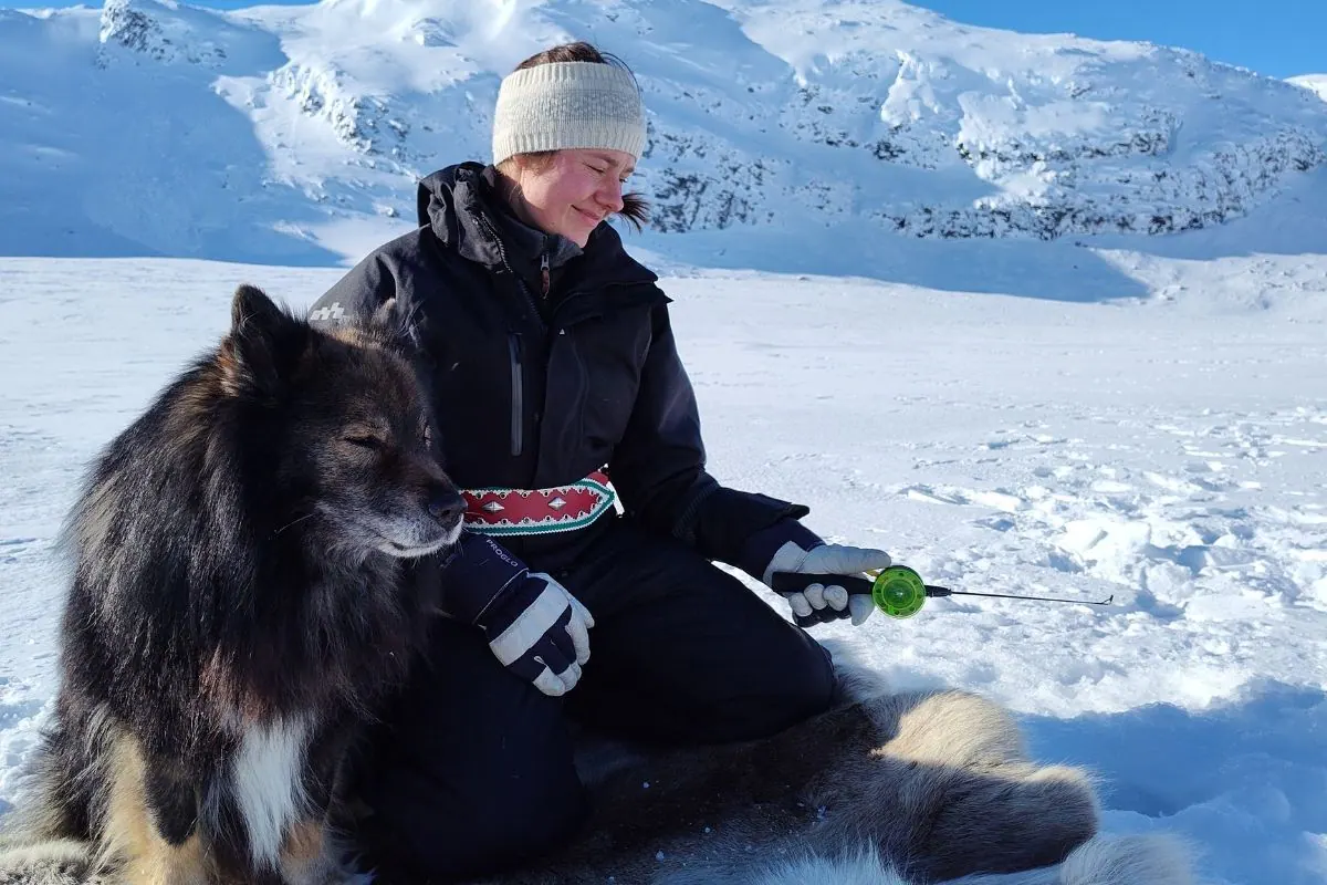 Woman and dog ice fishing on a sunny lake