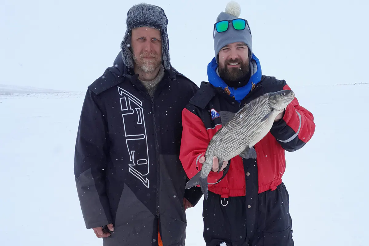 Two anglers holding a whitefish on a frozen lake