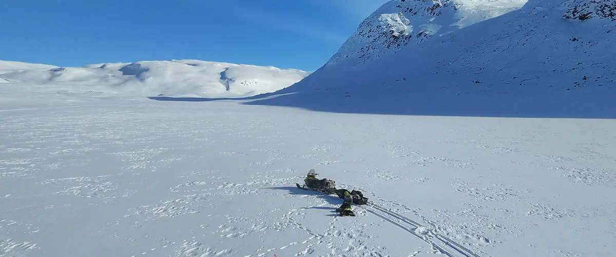 Snowmobile tracks on a frozen fell lake under bright spring sun