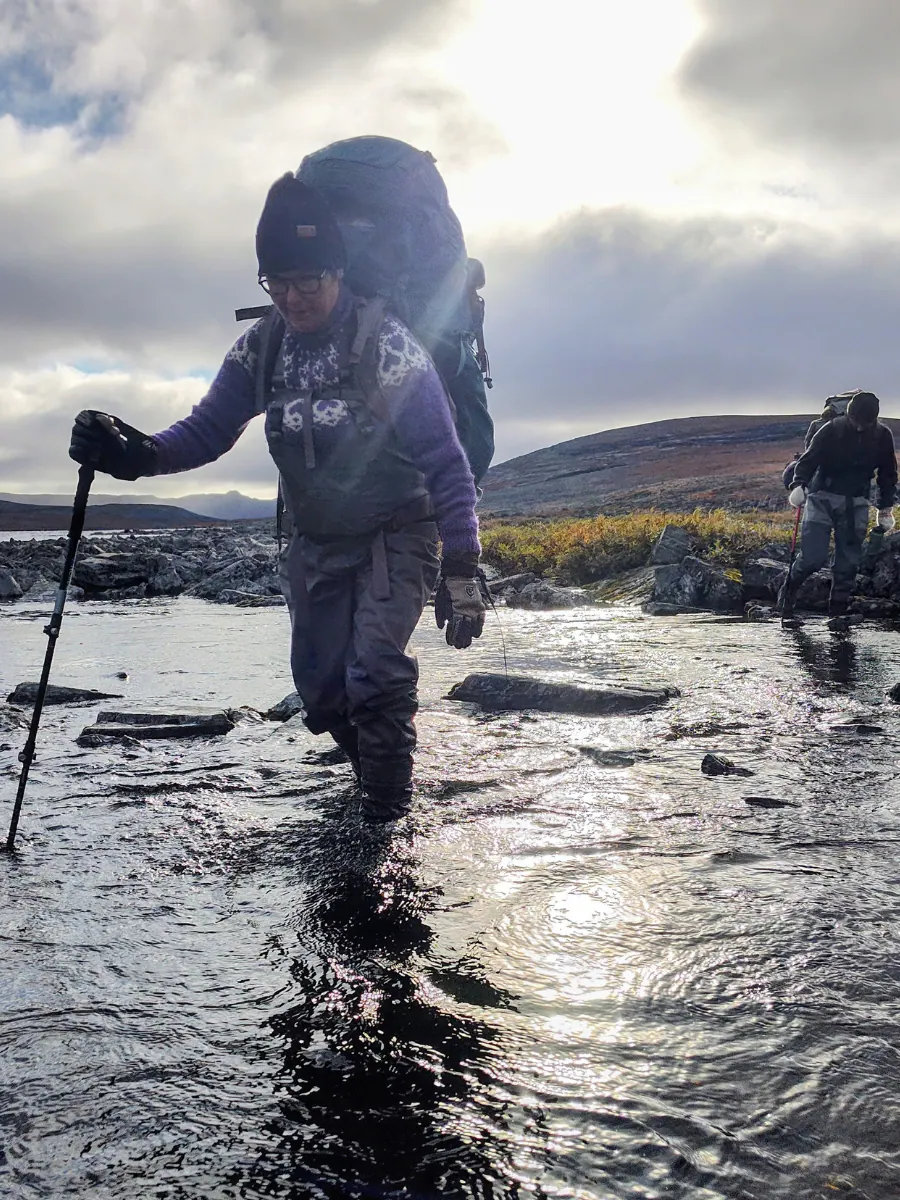 Angler wading a stony river with trekking poles