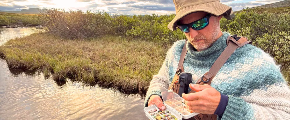 Teemu Vehviläinen choosing a fly from his fly box by the river