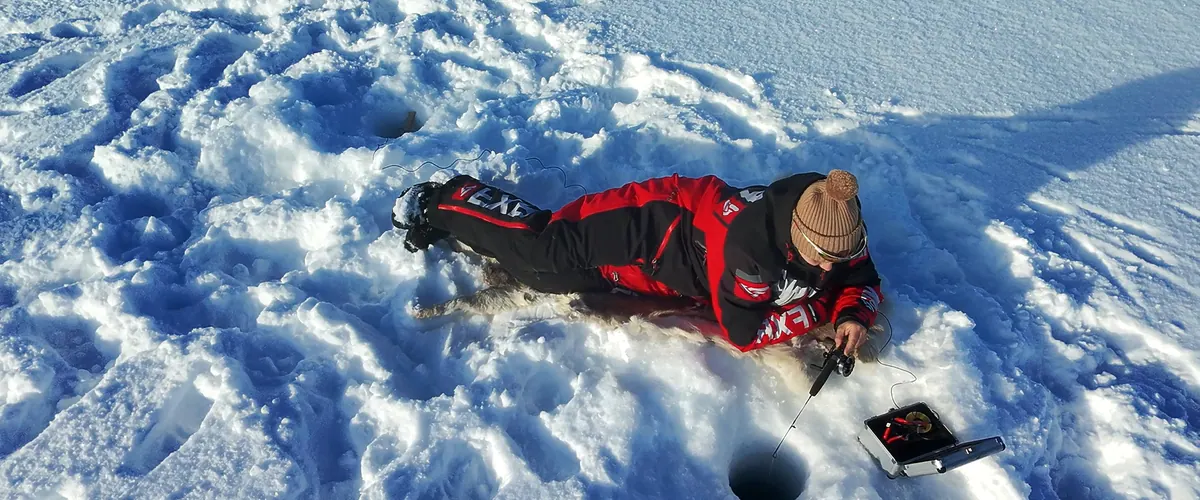 Angler lying on the snow looking into an ice hole