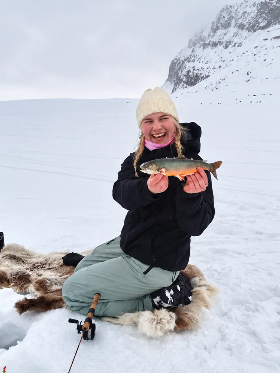 Smiling woman holding an Arctic char on the ice