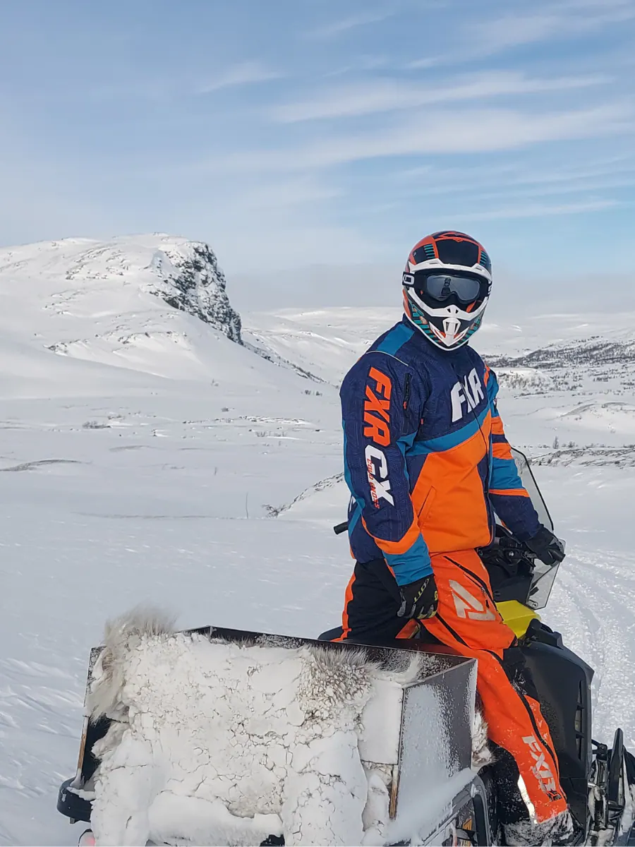 Angler in a snowmobile suit on a fell above a frozen lake