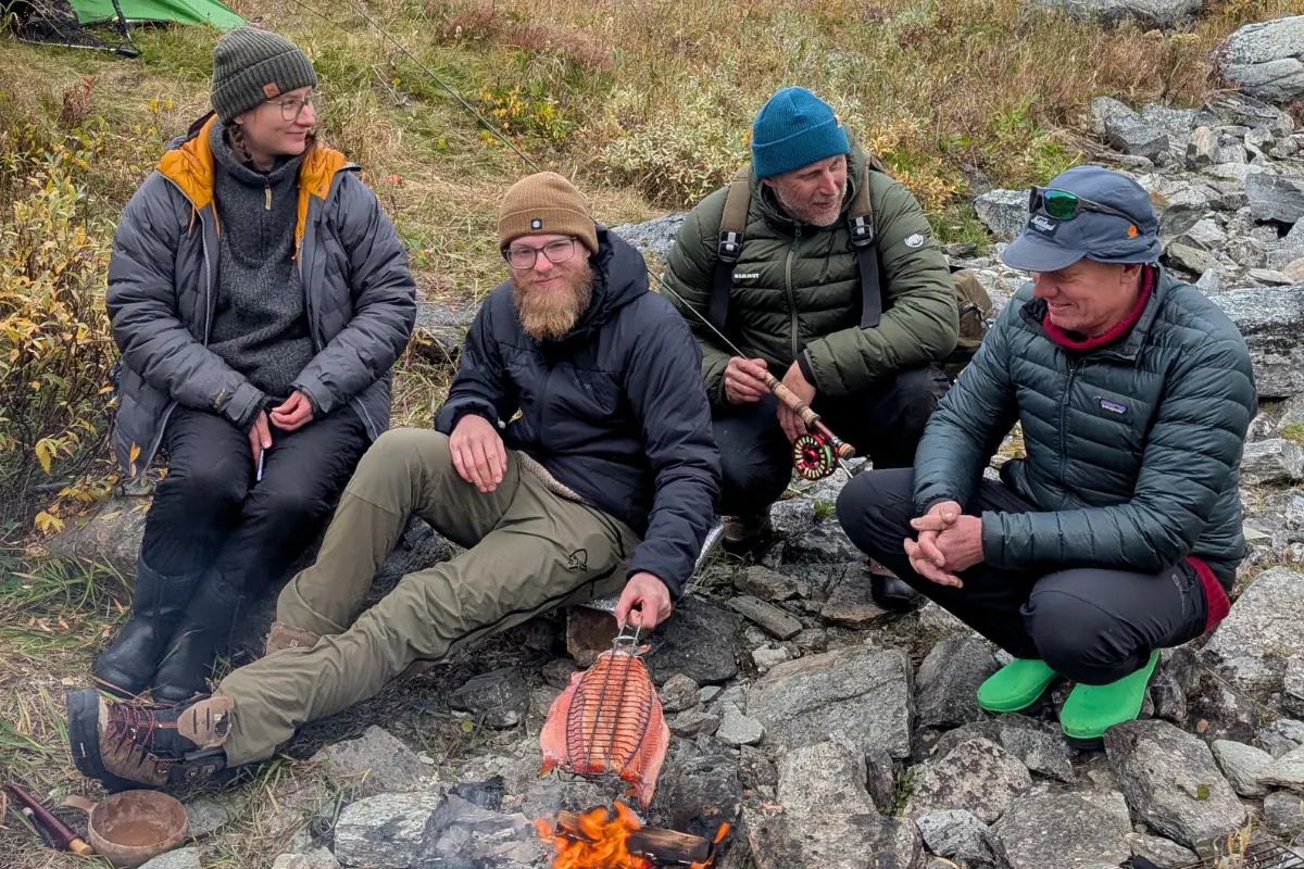 Teemu and guests by a campfire sharing a fish