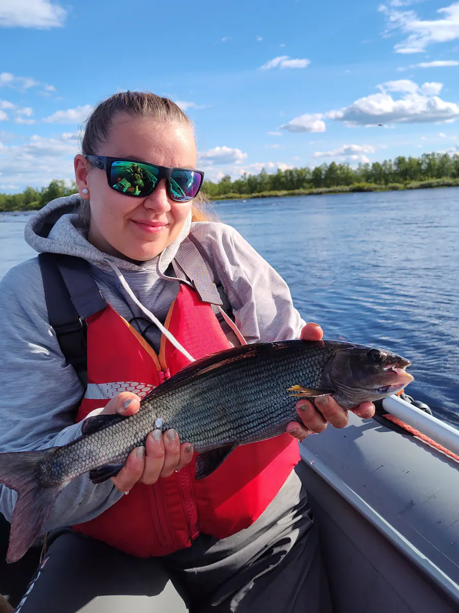 Woman angler holding a grayling in a boat