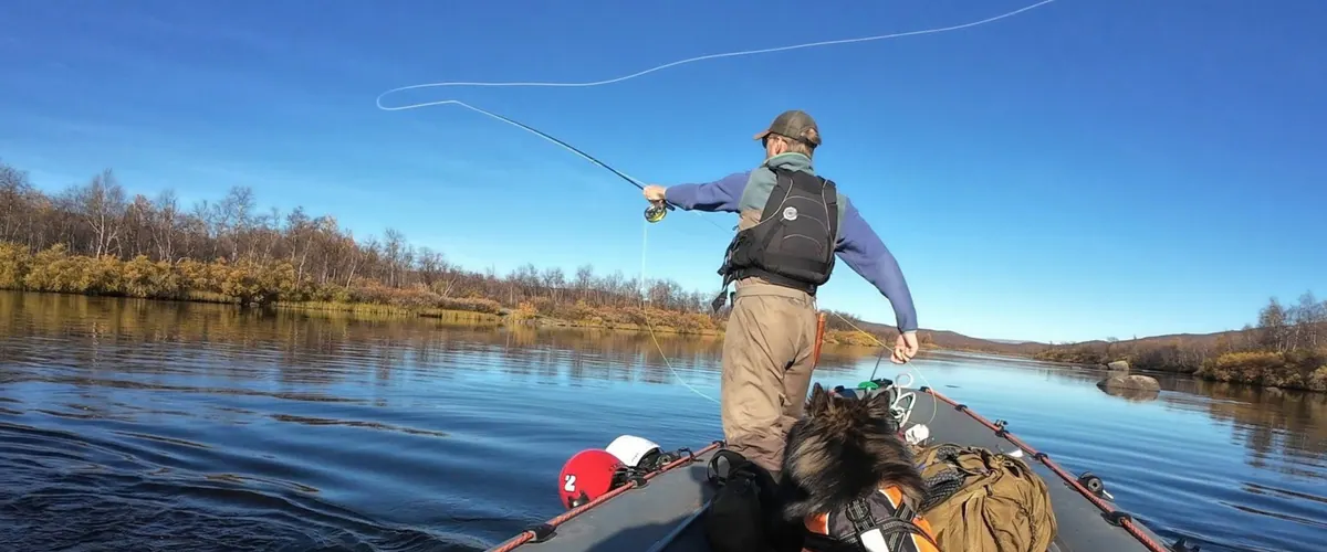 Fly fisher casting from a rubber boat at dusk