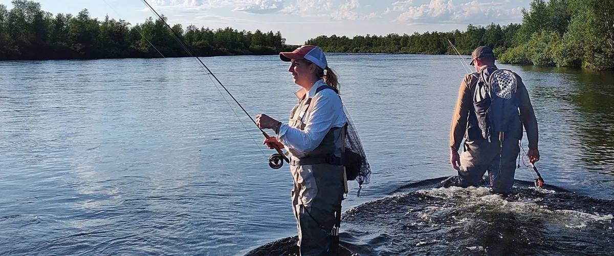 Two anglers fishing a calm river in the evening