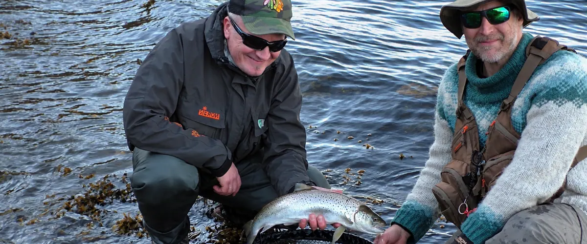Guide and guest releasing a sea trout on the shore