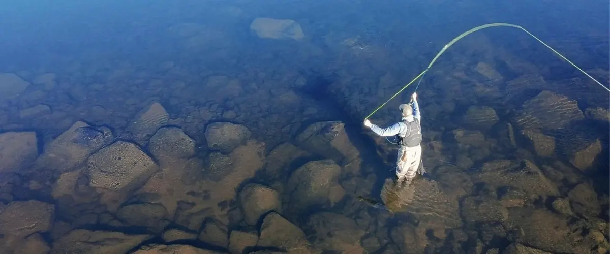 Angler casting from a stone in clear water
